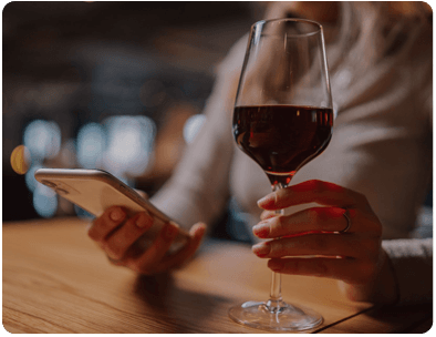 Persona sujetando una copa de vino mientras mira su tel�fono m�vil.